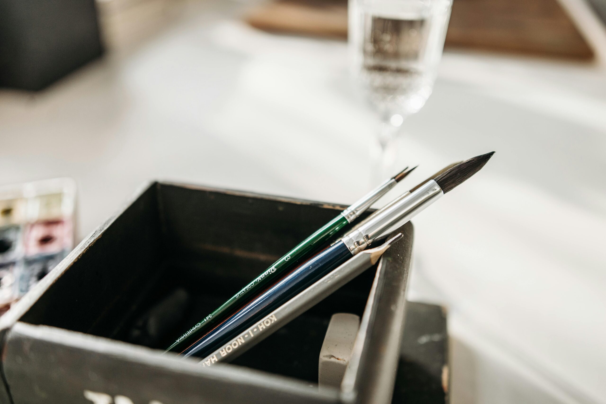 Detailed image of paintbrushes and pencil in a holder with soft light.